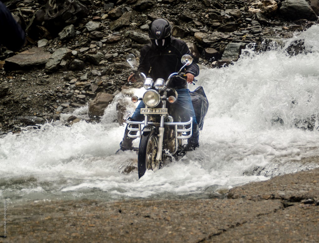 A biker navigates through a water crossing near Sarchu